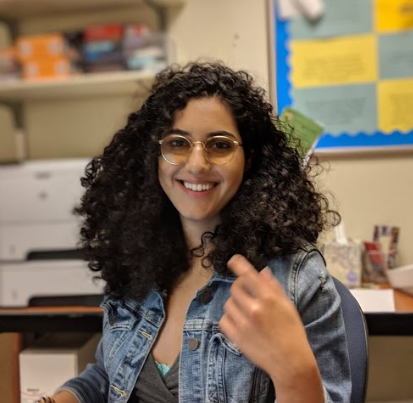 Smiling woman in classroom setting with glasses and curly hair.